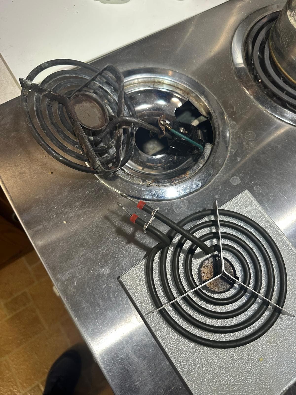 GE range repair in Alexandria, VA — A burned-out coil burner removed, burner socket exposed, and a new replacement burner element staged for installation