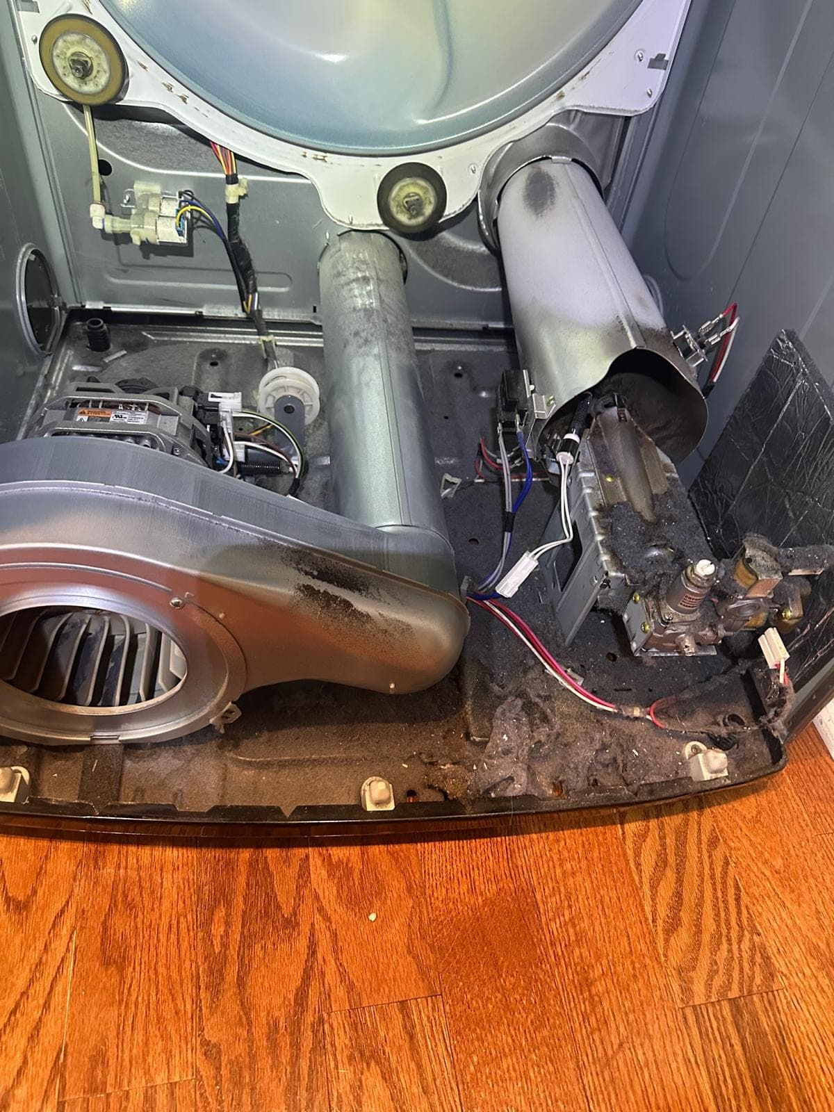 LG dryer repair in Alexandria, VA — The base panel removed, exposing a heavily lint-clogged blower wheel, gas valve assembly, and exhaust duct
