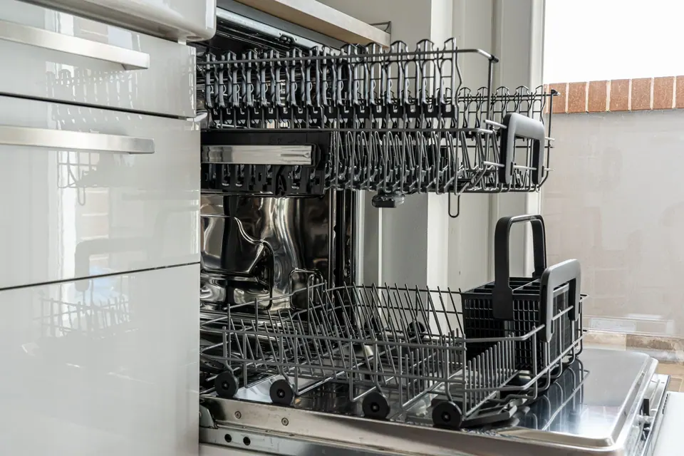Open dishwasher with empty racks pulled out in a modern white kitchen
