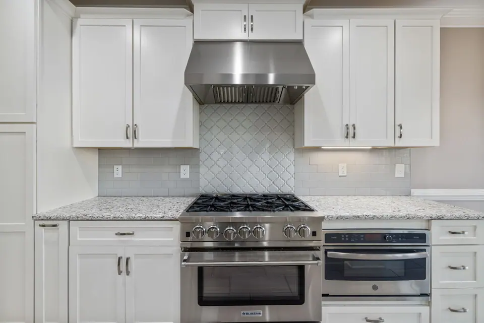 Stainless pro-style gas range with oven below and hood in a white kitchen