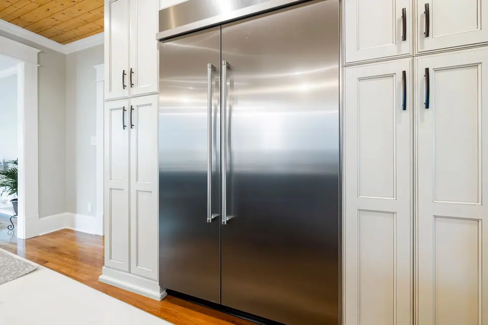 Built-in stainless steel refrigerator between white cabinets in a bright kitchen