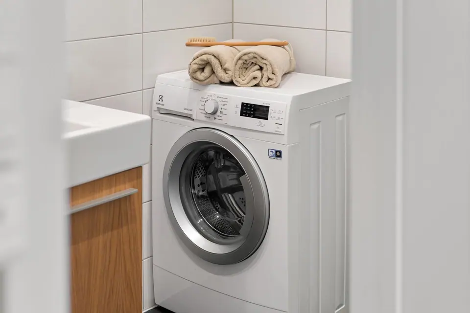 White front-load washing machine with folded towels in a tiled laundry