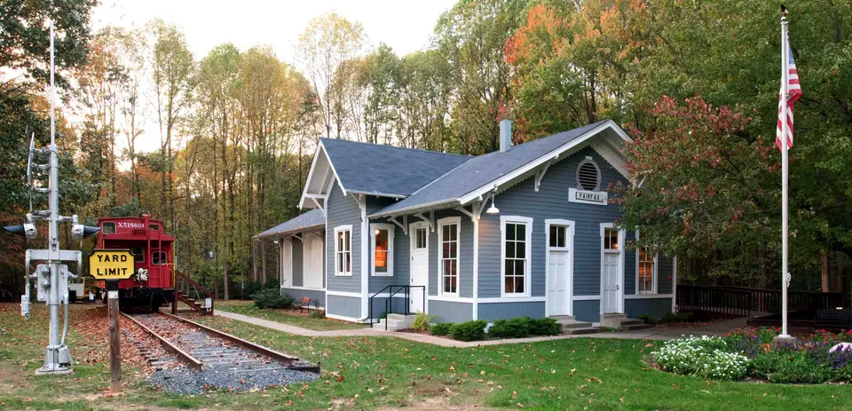The Fairfax Station Railroad Museum in Fairfax Station, Virginia: the restored grey depot building with a red caboose on the track beside it, surrounded by autumn trees