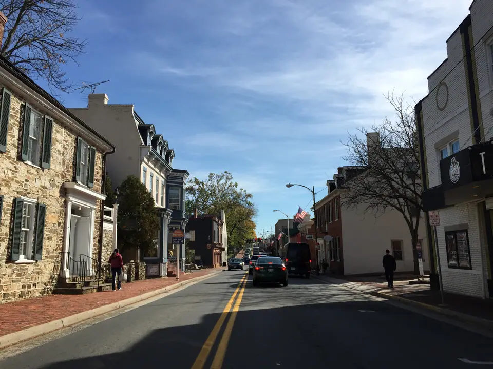 Market Street in downtown Leesburg, Virginia, looking east toward King Street past historic stone and brick storefronts on a sunny autumn day
